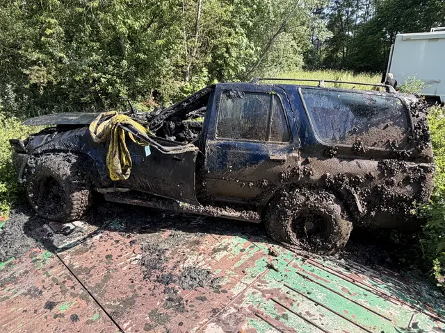 Ein über und über mit Muscheln und Lehm bedeckter, stark beschädigter, schwarzer Geländewagen. Das Dach ist über der Windschutzscheibe stark eingedrückt. An dem Fahrzeug befindet sich ein gelbes Band, das zur Bergung verwendet wurde. 